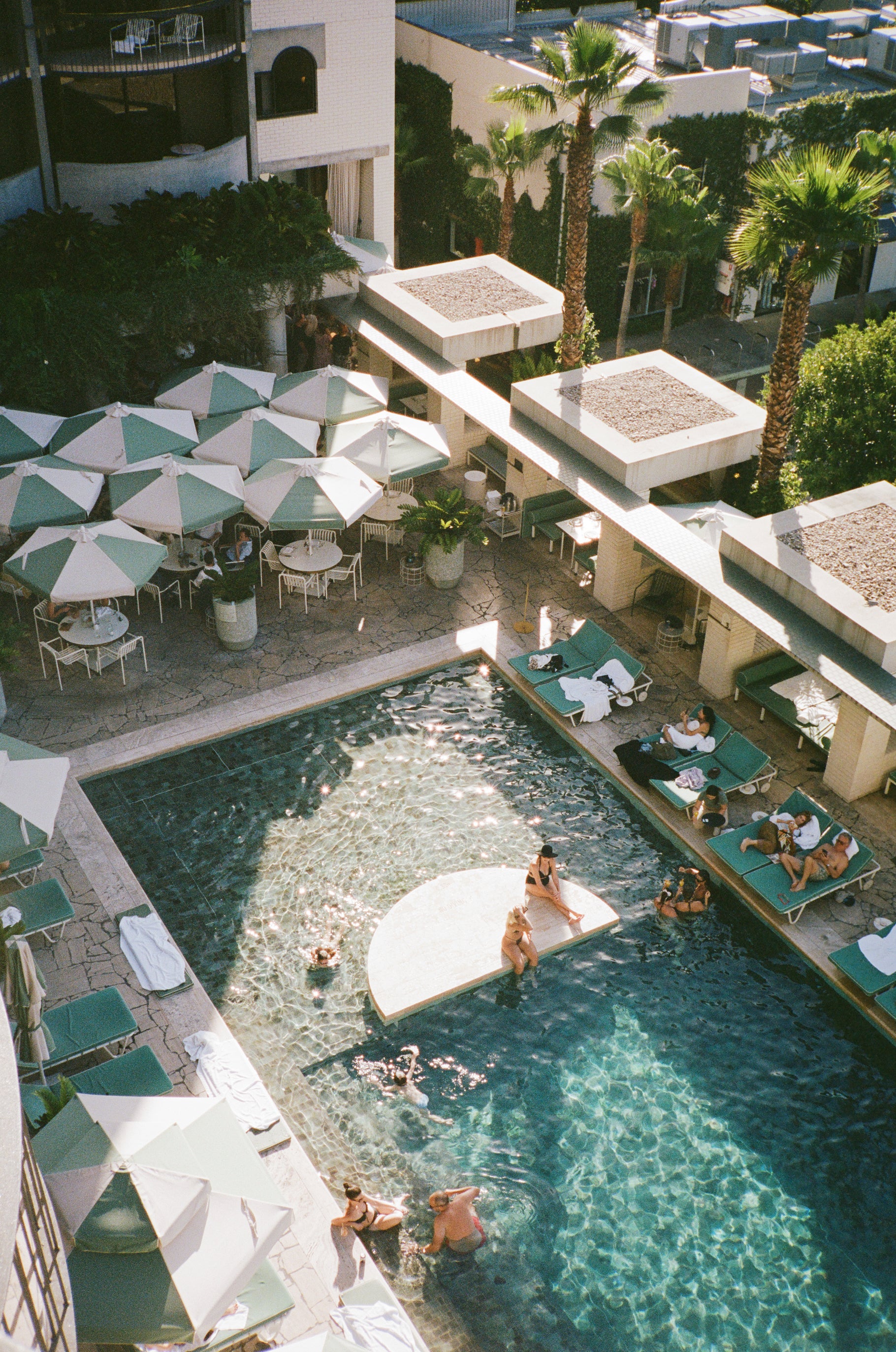 Ariel photograph of the Calile Hotel's pool with swimmers and sunbathers on sun lounges under umbrellas.