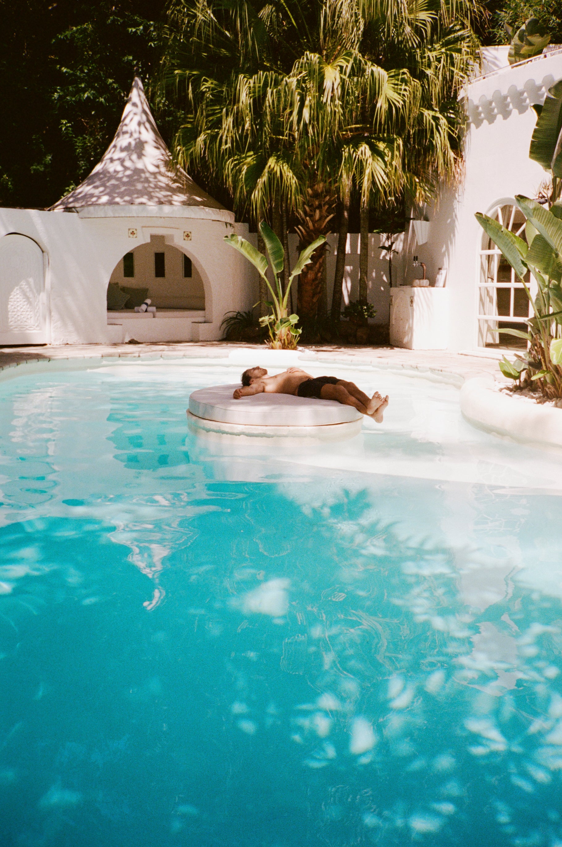 Photograph of a man sunbathing on a lounge floating in a pool in the backyard of a boutique hotel in Byron Bay called Raes Wategos.