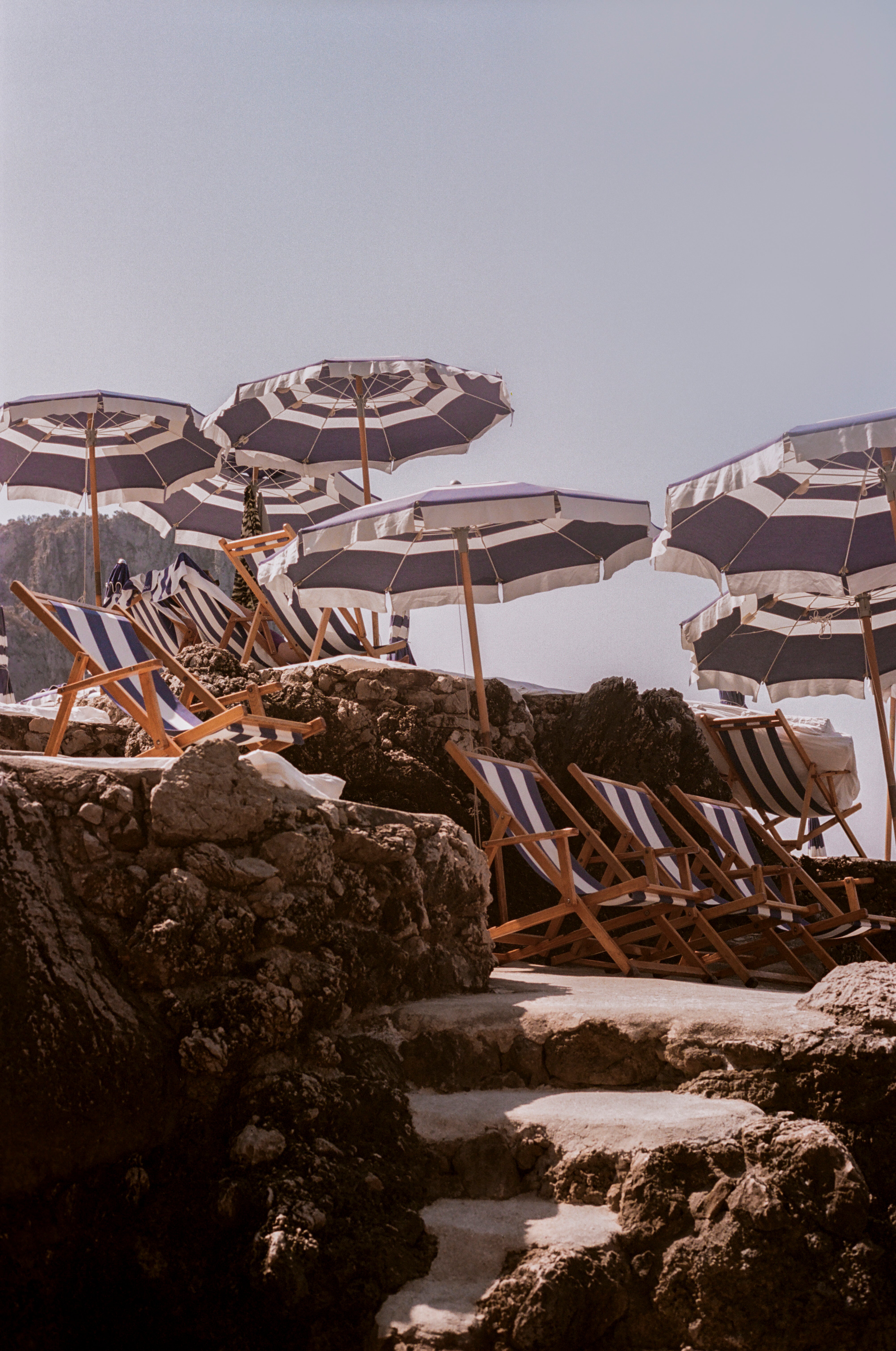 Photograph of blue and white umbrellas and sun lounges at La Fontelina beach club in Capri, Italy.