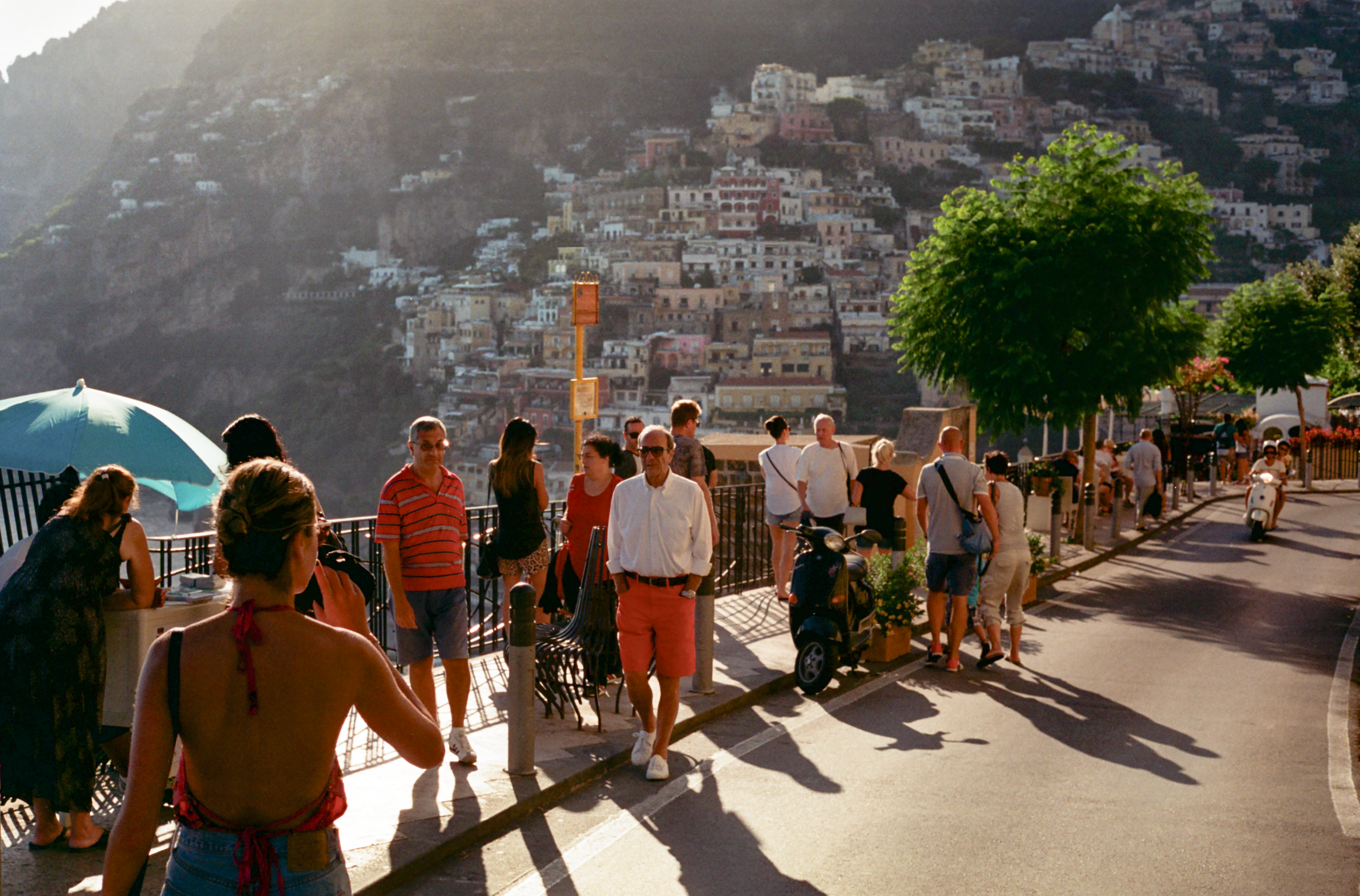 Photograph of the iconic Positano cliffside at sunset with tourists and locals walking and a motorbike driving.